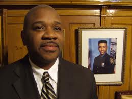 District Leader Geoffrey Davis with a photo of his brother, the Late City Councilman James E. Davis behind him (courtesy of the New York Times)