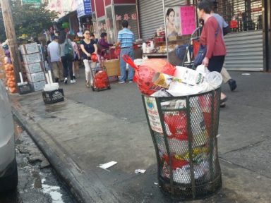 An overflowing trash can lines one of the corners on Eighth Avenue in Sunset Park. City Councilman Carlos Menchaca last week announced $200,000 in additional sanitation funding to help keep corner waste baskets from crowding  busy corridors in Sunset Park and Red Hook.   Photo by Heather Chin.