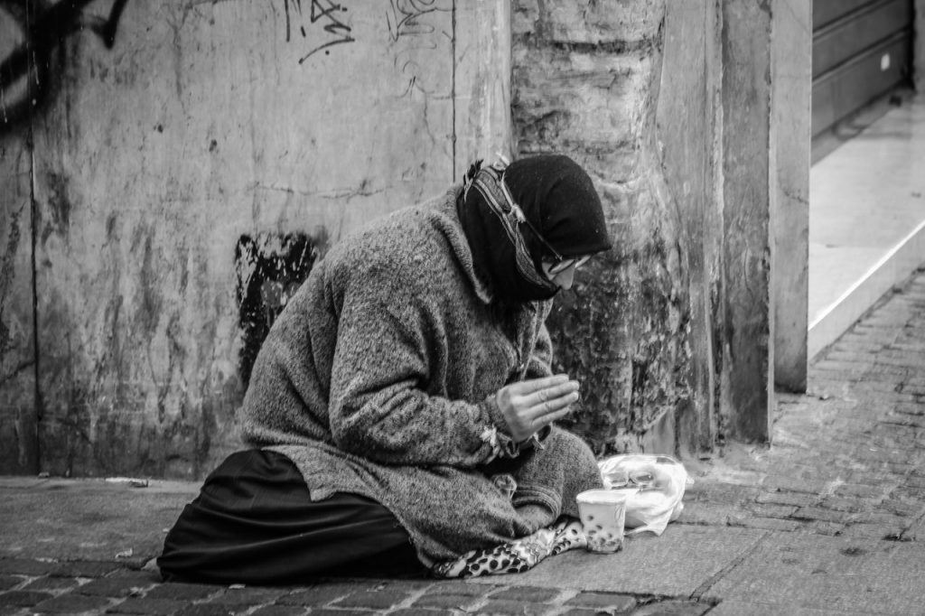 grayscale-photography-of-man-praying-on-sidewalk-with-food-1058068
