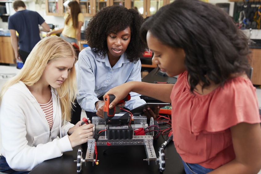 Teacher With Female Pupils Building Robotic Vehicle In Science Lesson