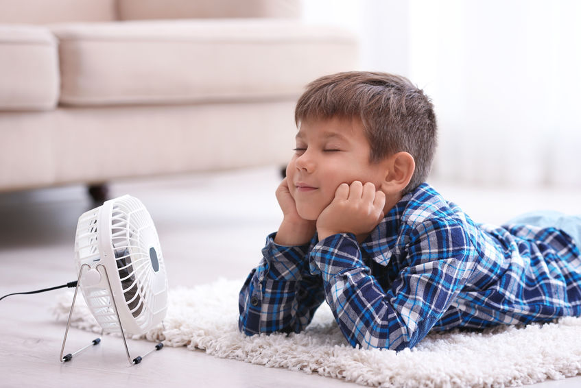 Little boy refreshing from heat in front of small fan at home