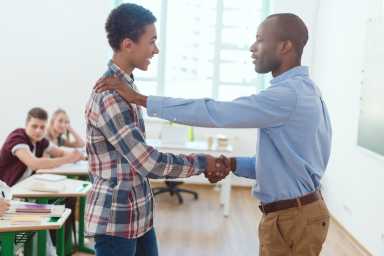 Side view of african american teacher shaking of high school teenage student in clasroom