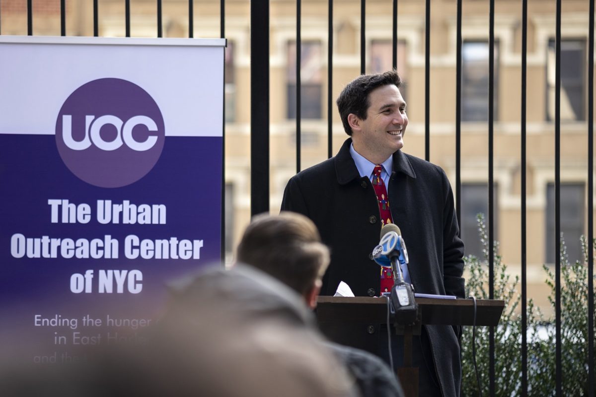 Council Member Ben Kallos smiling during his speach with "The Urban Outreach Center of NYC" banner behind him.