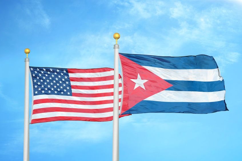 United States and Cuba two flags on flagpoles and blue cloudy sky