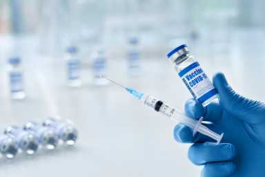 Male doctor hand wears glove holding syringe and vial with covid 19 vaccine.