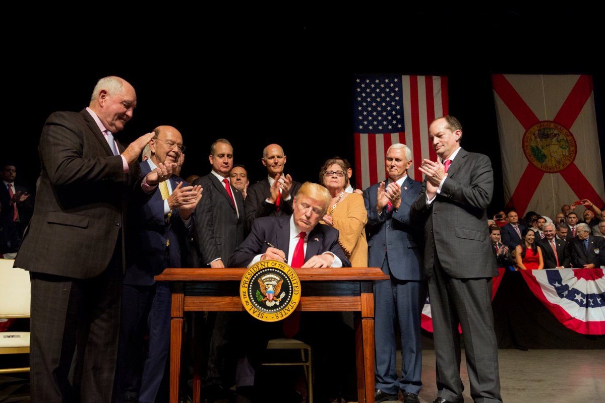 Trump signing the memorandum on a stage surrounded by fellow republican lawmakers.