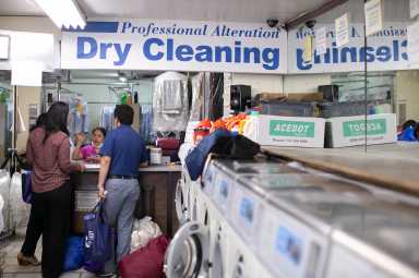 Inside a local laundromat, two customers speaking to an employee at the counter