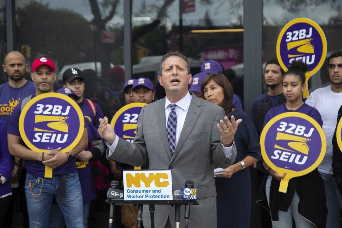 Councilman Bradlander speaking in front of fast food prosters holding "32BJ SEIU" signes.