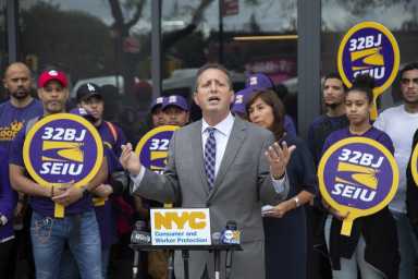 Councilman Bradlander speaking in front of fast food prosters holding "32BJ SEIU" signes.