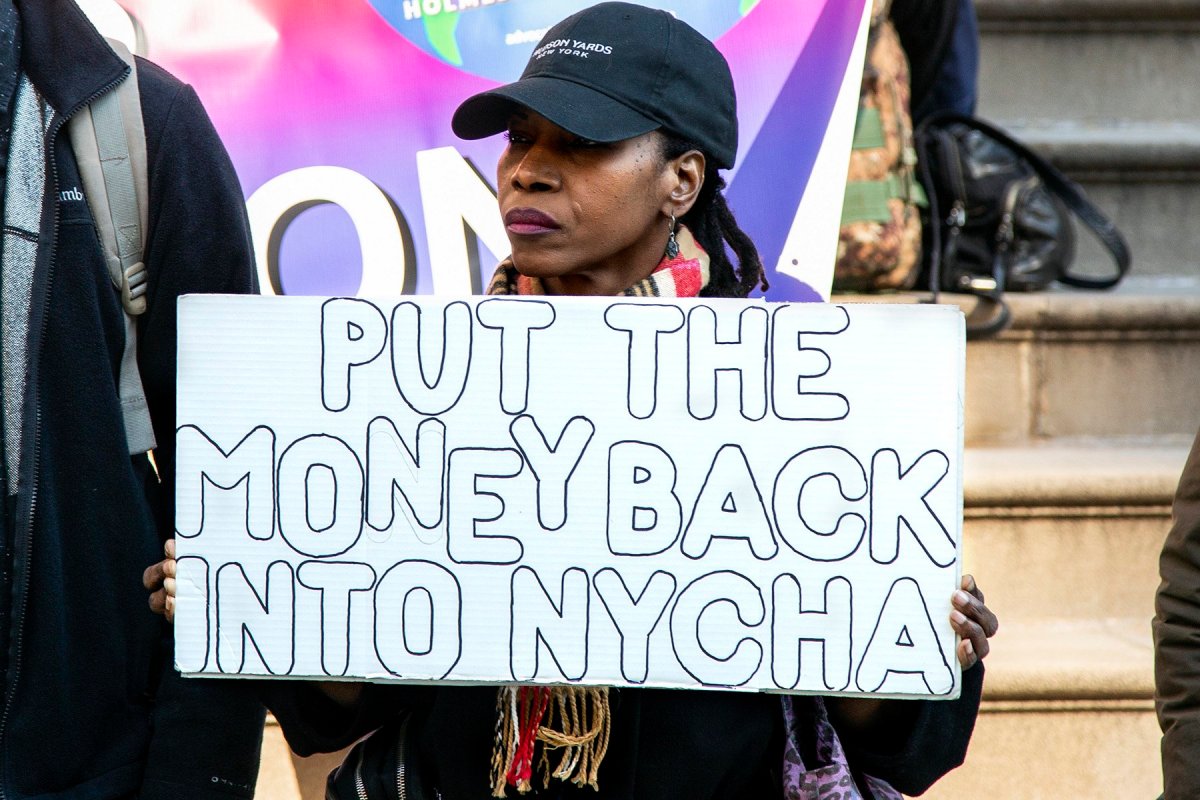 A woman holding a sign that reads "Put the Money Back Into NYCHA"