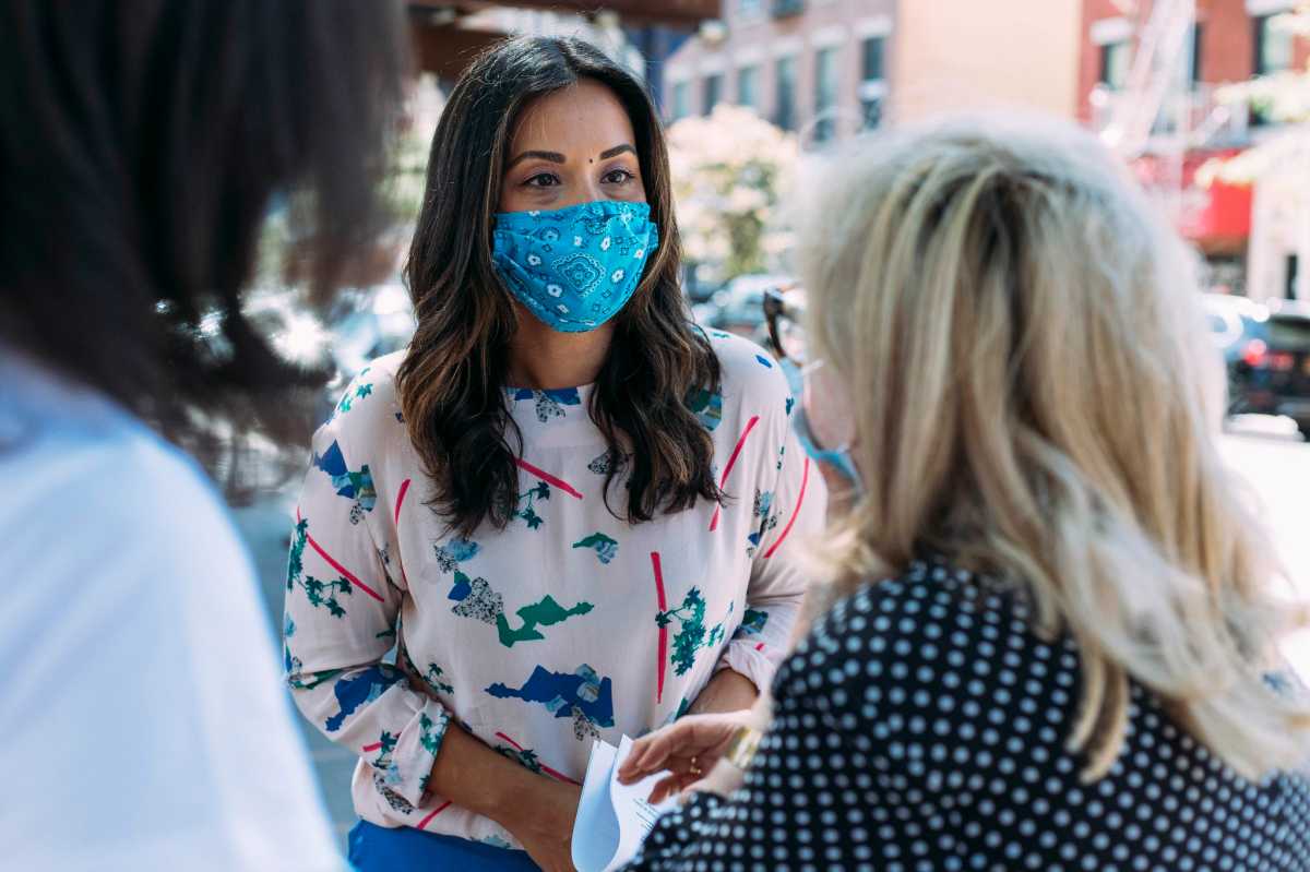 Council Member Carlina Rivera with mask over her mouth/nose speaking to a woman.