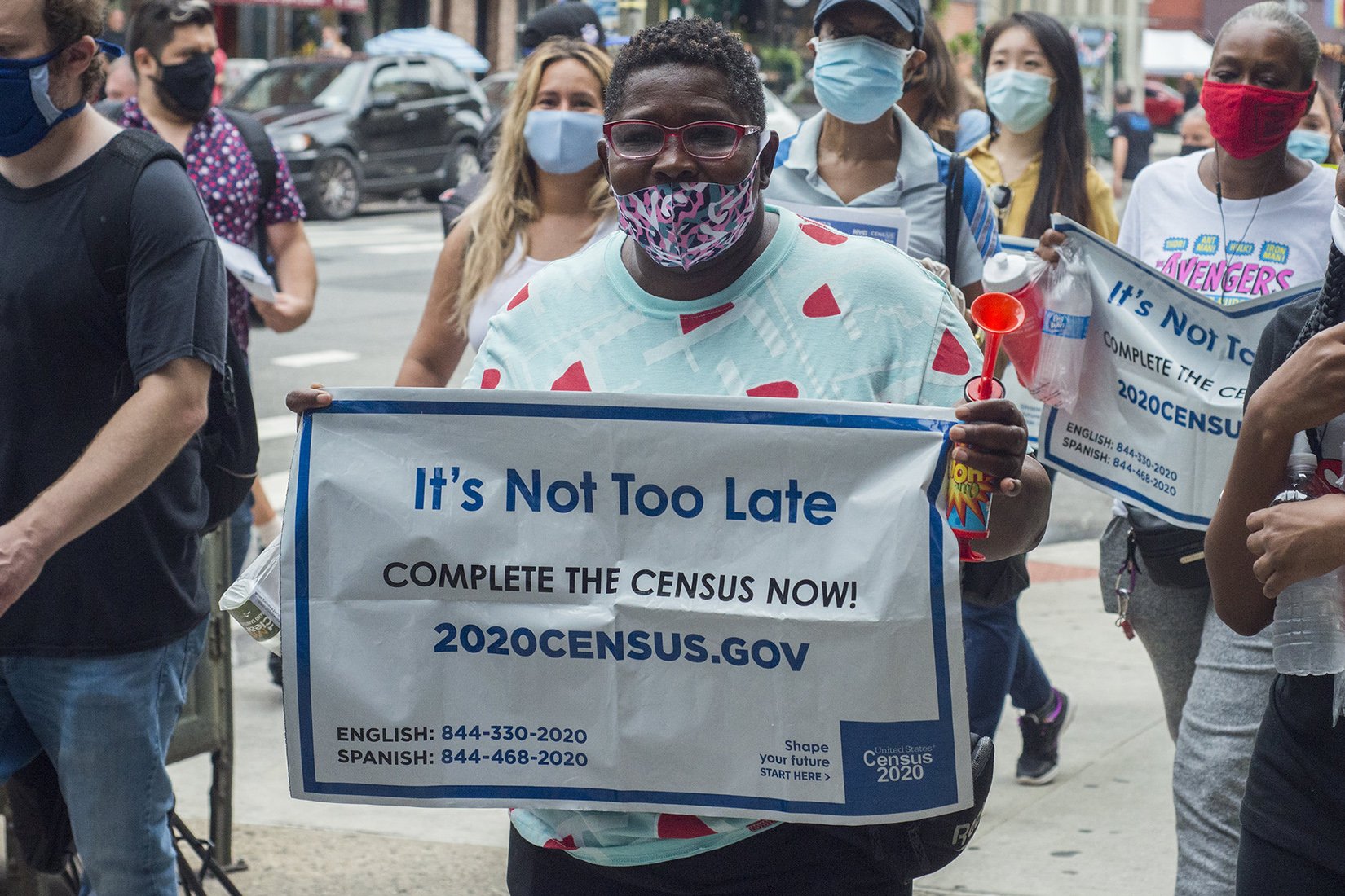 A participant at the march holding a sign to the camera that says, "It's not too late, complete the census now! 2020census.gov"