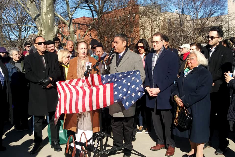 Adriano Espaillat speaking to the crowd with an American flag in his hand.