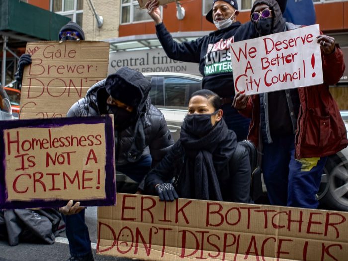 Marni Halasa and protesters holding signs on the street. The signs read, "Homelessness is not a crime!" "Erik Bottcher don't displace us!" "We deserve a better City Council!" "Hon. Gale Brewer: Don't cave.."