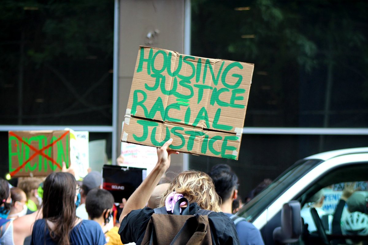A man holding a sign "Housing Justice = Racial Justice" cardboard sign at a protest