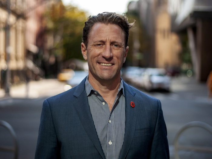 Zach Iscol in suit, outdoor on a street in New York, a slight smile to the camera